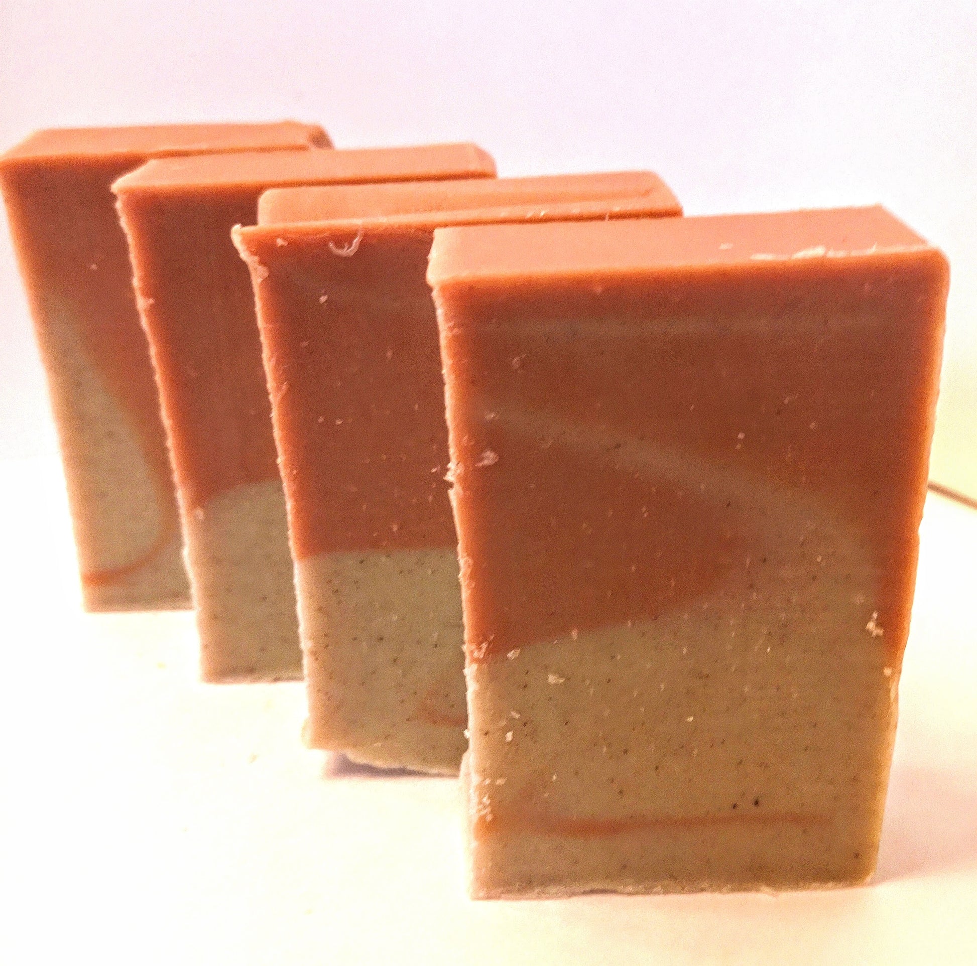 Four bars of soap on white background. Pink on upper half and peach coloured on lower half with swirl in middle of the bar. 