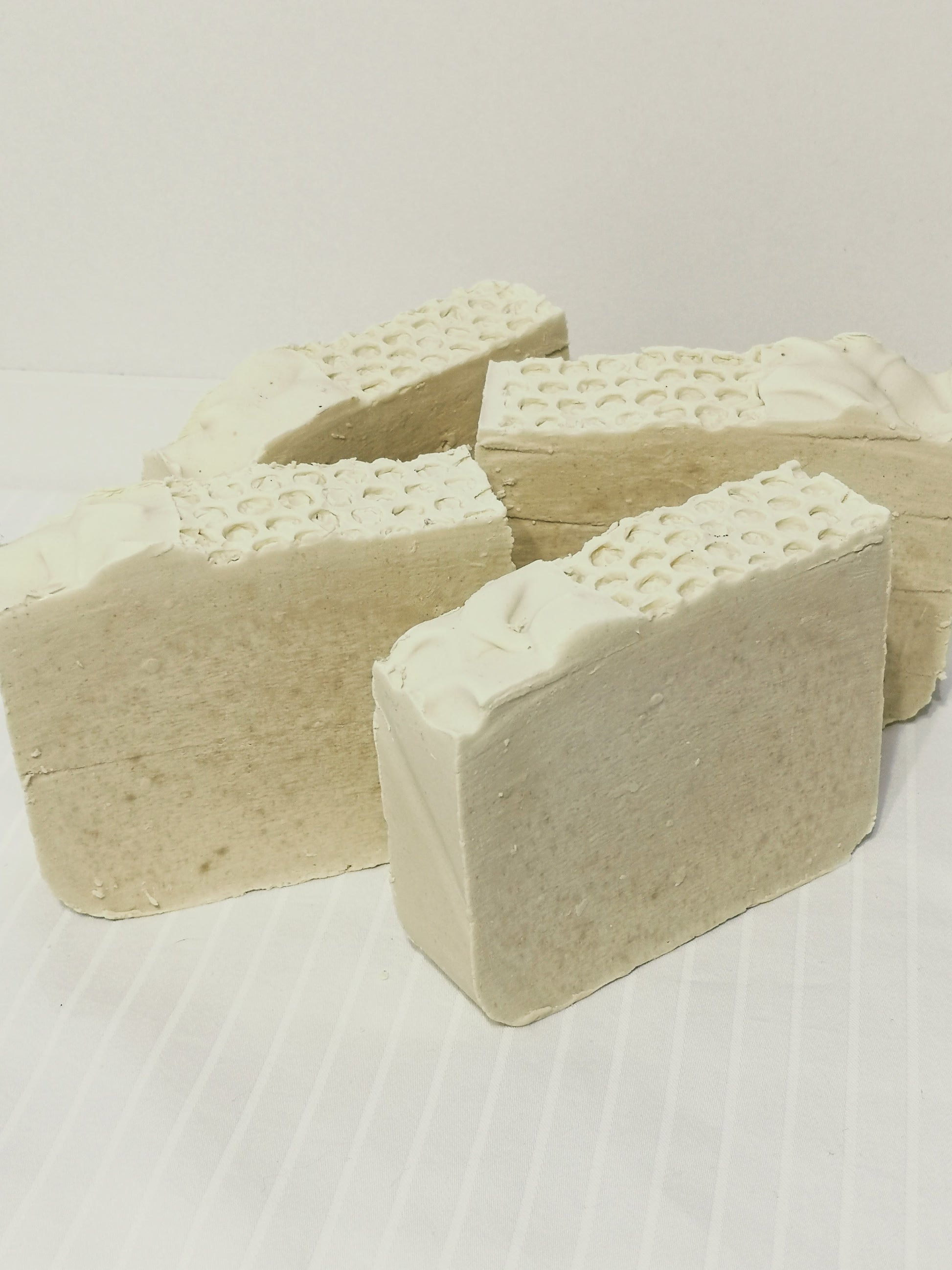 4 bars of creamy white soap with textured top on an off-white background. 