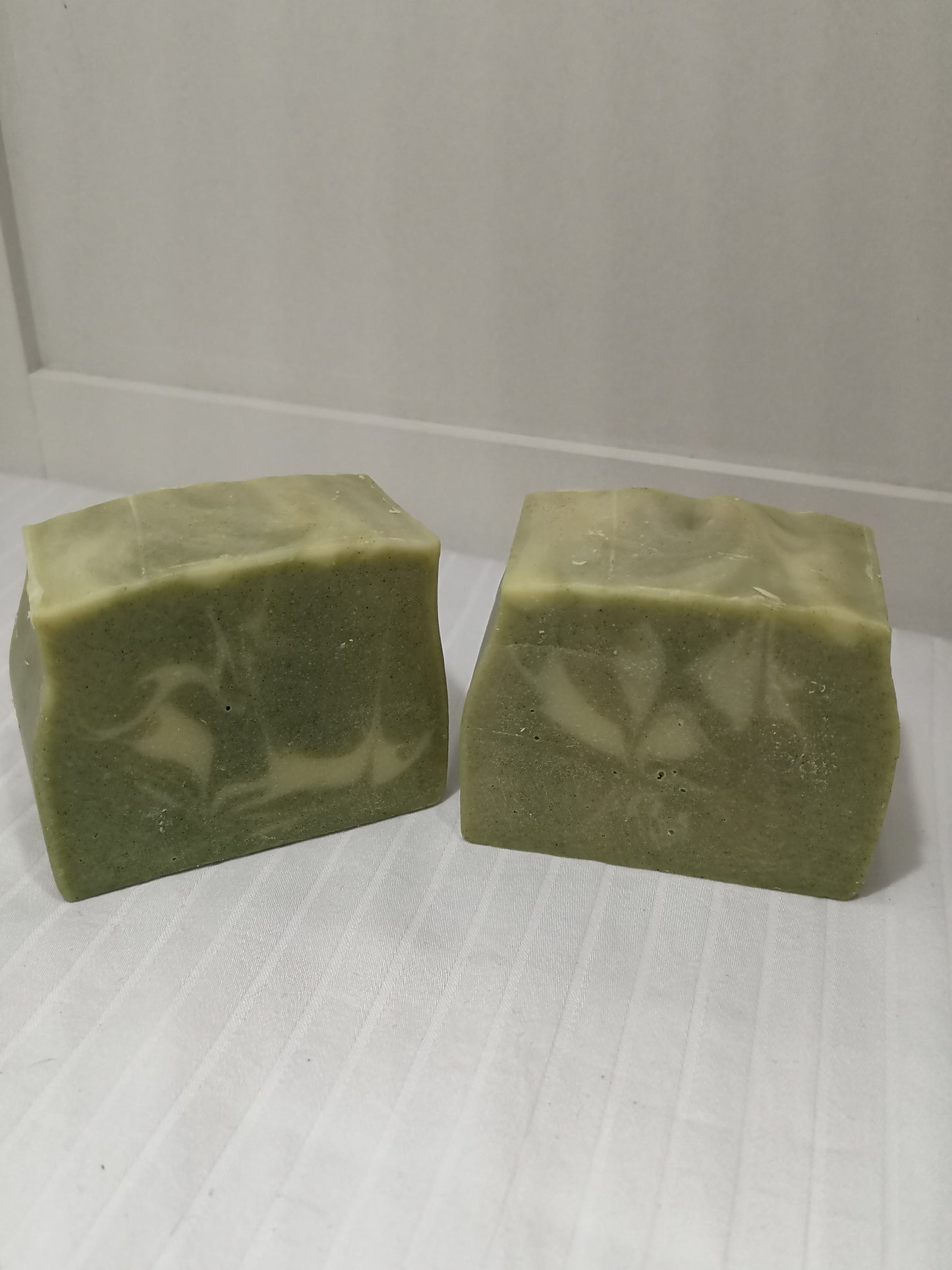 Two bars of green soap with white swirl feature on an off-white background. 