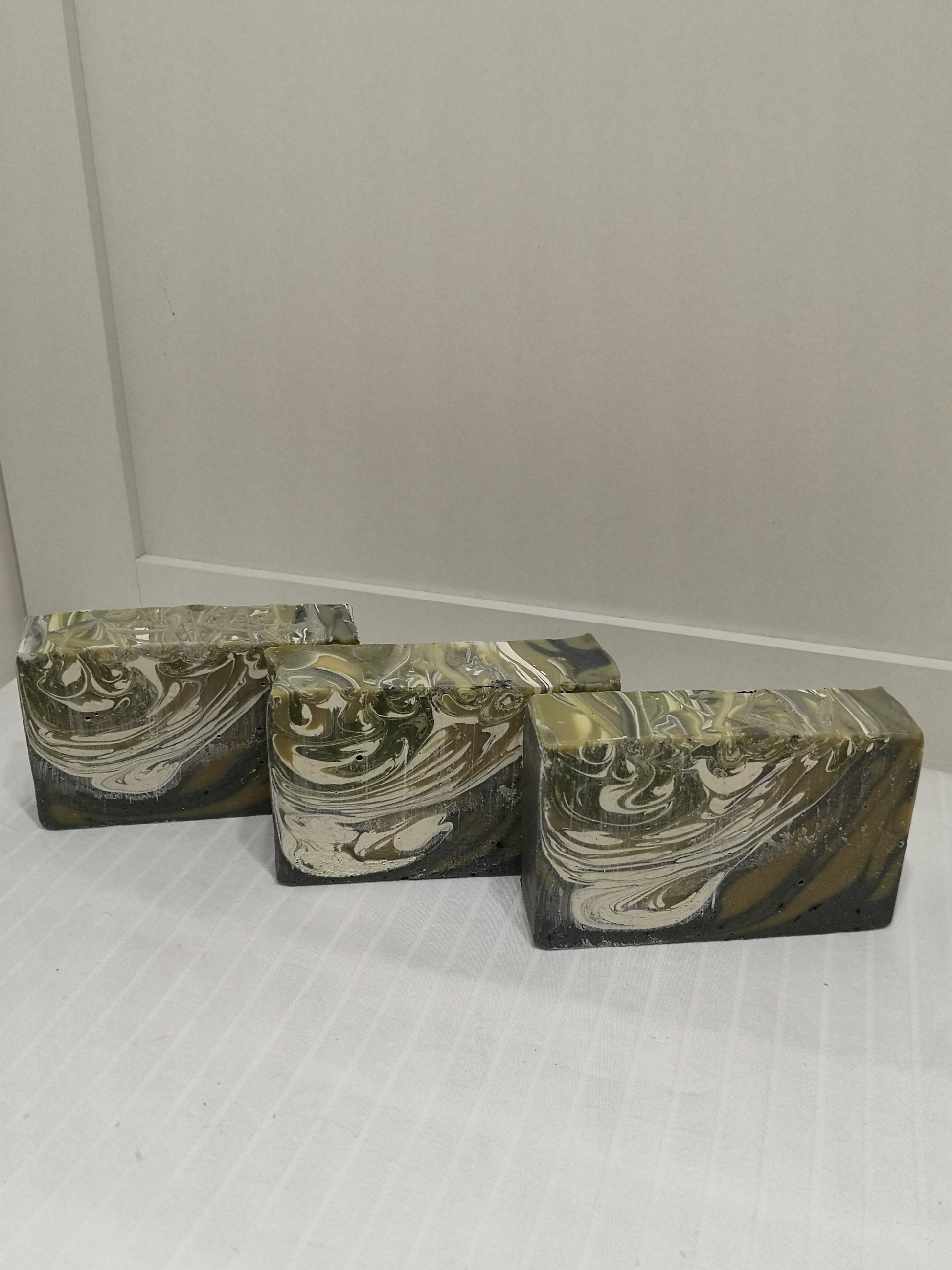Three bars of soap on an off-white background. Black, brown and cream swirl.